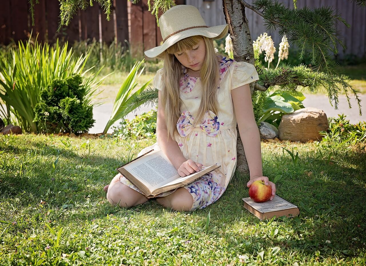 Dziecko, które siedzi na trawie i czyta książkę